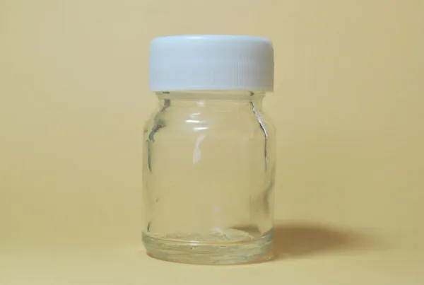 Person examining nootropic supplement bottle with magnifying glass in home office, surrounded by pill bottles and health docu